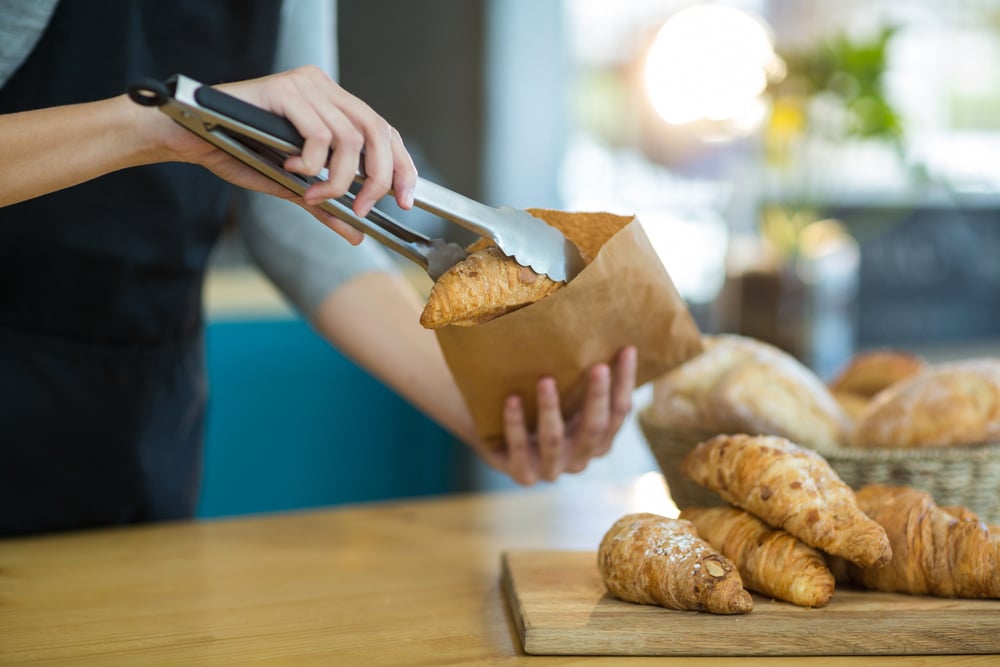 Mid-section of waitress packing croissants in paper bag at cafx92xA9